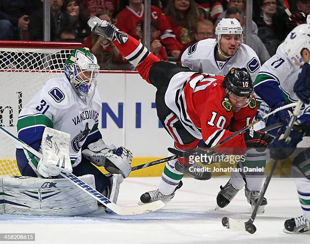 Patrick Sharp of the Chicago Blackhawks falls to the ice between Eddie Lack and Christopher Tanev of the Vancouver Canucks at the United Center on...