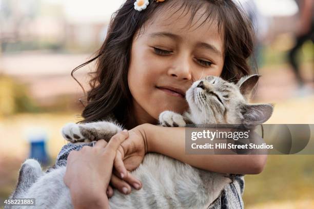 hispanic girl cradling cat - cute animals cuddling stock-fotos und bilder