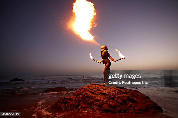 woman breathing fire on rocky beach - zirkuskünstler stock-fotos und bilder