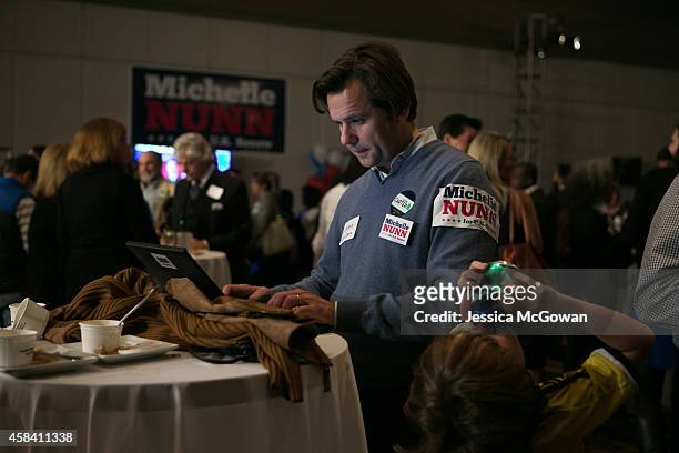 As his son Oscar Garcia-Ide finishes a can of soda, Humberto Garcia-Sjogrim checks election results data during the election party for Georgia...
