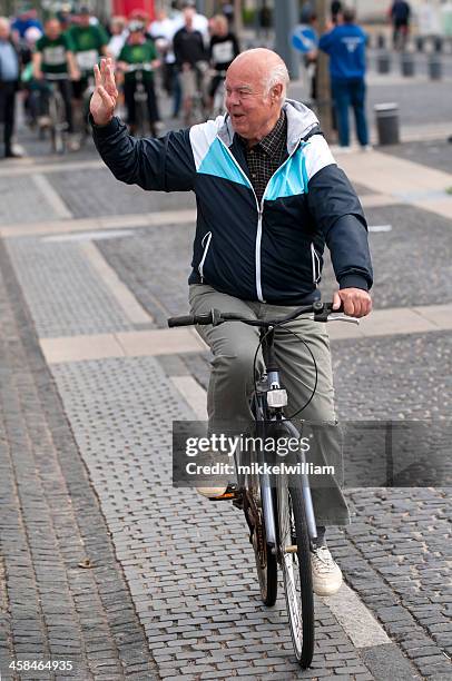 senior citizen rides a bicycle and waves his hand - zwaaien gebaren stockfoto's en -beelden