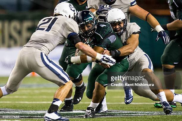 Steven Lakalaka of the Hawaii Warriors is stopped by Brian Suite and LT Filiaga of the Utah State Aggies during the third quarter of a college...