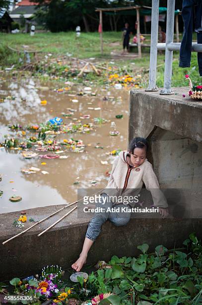 Thai girl waits for her mother on a floodgate while searching for valuables from krathongs in the Ping river after Loy Krathong Festival in Chiang...