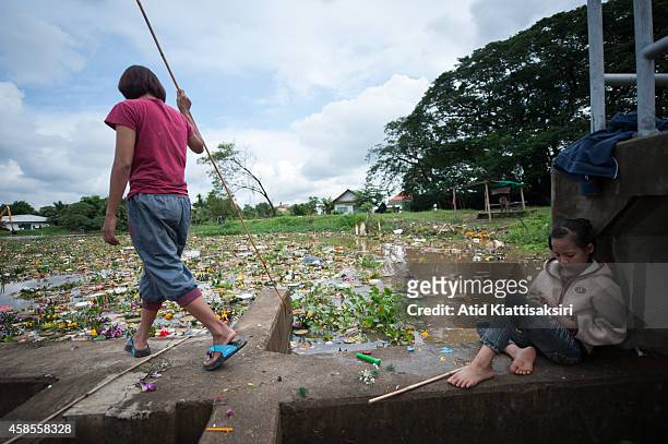 Thai girl plays with a smart phone as she waits for her mother who is finding valuables from krathongs on the Ping river after the Loy Krathong...