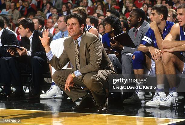 Kentucky coach Rick Pitino squatting in front of bench during game vs Louisville at Freedom Hall. View of Kentucky assistant coaches Bernadette Locke...