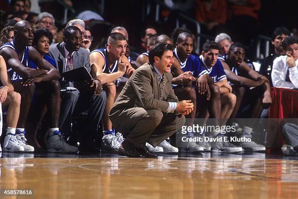 Kentucky coach Rick Pitino squatting in front of bench during game vs Louisville at Freedom Hall. View of Kentucky assistant coach Bernadette Locke...