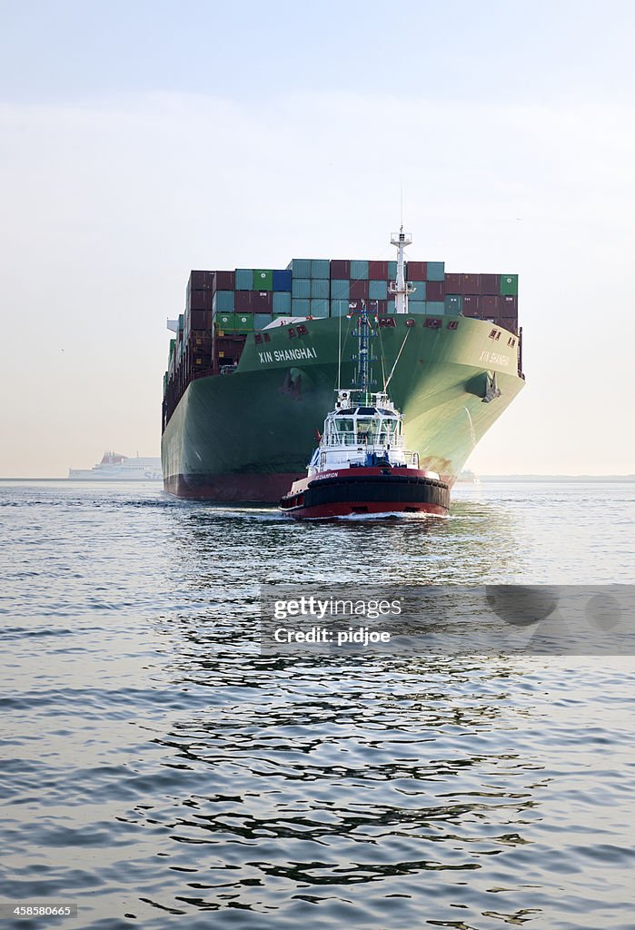 Tugboat towing cargo container ship into harbor