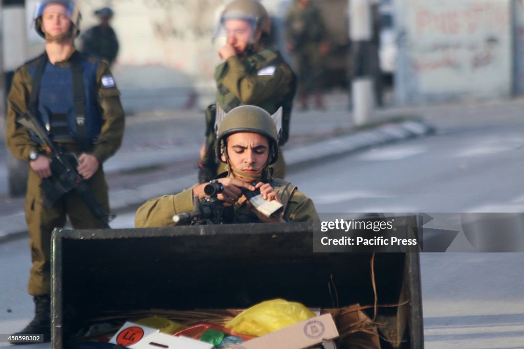 An Israeli soldier, crouched behind a trash bin, reloads his...