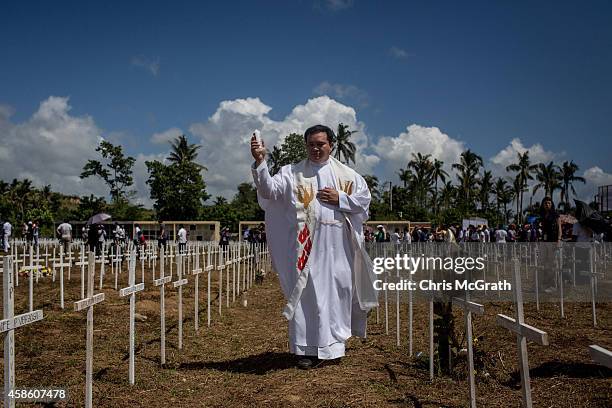 Parish priest blesses the gravesites of typhoon victims during a memorial service at the mass grave on the grounds of the Holy Cross Memorial Garden...