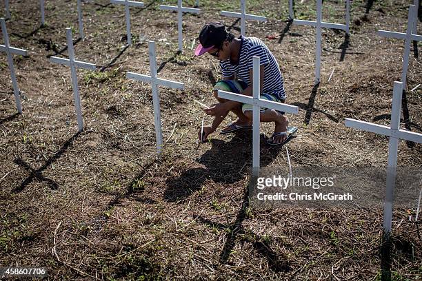 Lights candles at the cross of a loved one at the mass grave on the grounds of the Holy Cross Memorial Garden on November 8, 2014 in Tacloban, Leyte,...