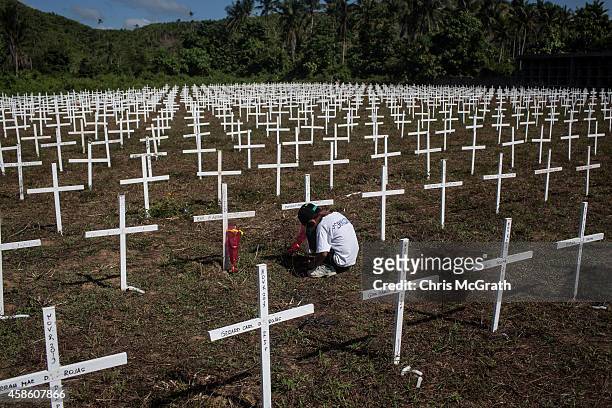 Young boy sits at the cross of a loved one at the mass grave on the grounds of the Holy Cross Memorial Garden on November 8, 2014 in Tacloban, Leyte,...