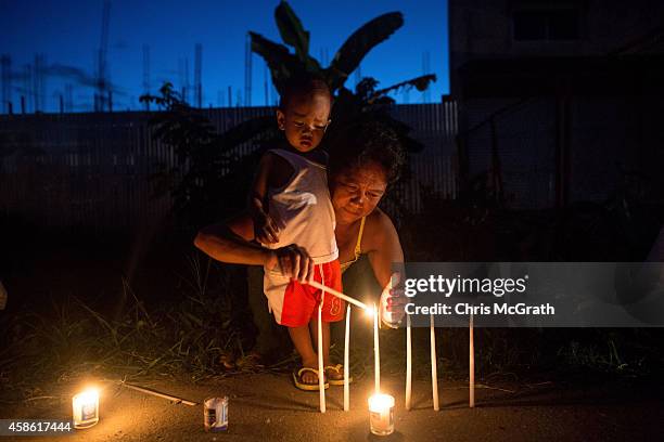 Woman and her child light a candle on the roadside in San Jose during the candlelight memorial on November 8, 2014 in Tacloban, Leyte, Philippines....