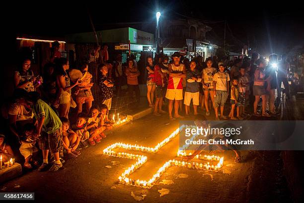 People gather on the street around candles shaped in a cross during the candlelight memorial on November 8, 2014 in Tacloban, Leyte, Philippines....
