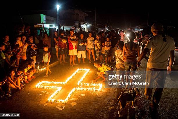 People gather on the street around candles shaped in a cross during the candlelight memorial on November 8, 2014 in Tacloban, Leyte, Philippines....