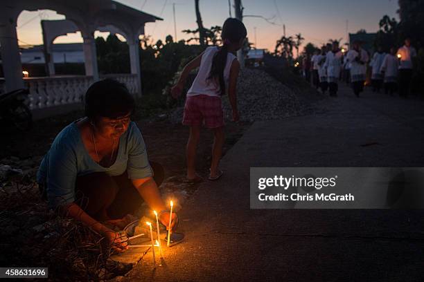 Evelyn Factoranan, who lost 28 relatives in the typhoon places candles on the street outside her home as residents of San Joaquin walk past during a...