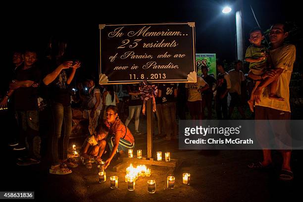 People stand around a memorial sign during the candlelight memorial on November 8, 2014 in Tacloban, Leyte, Philippines. People lined the roads with...