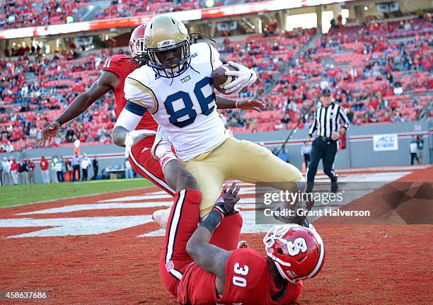 Darren Waller of the Georgia Tech Yellow Jackets beats defenders Mike Stevens and Germaine Pratt of the North Carolina State Wolfpack during their...