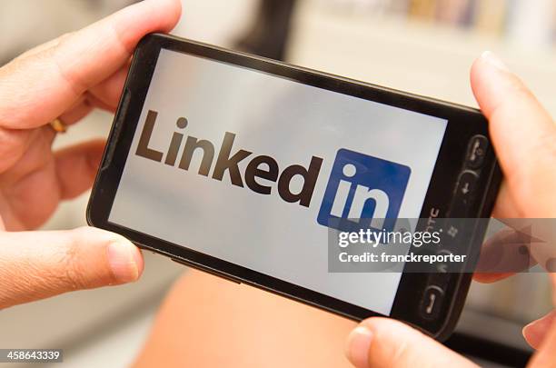mujer sosteniendo un smartphone con logotipo de linkedin - medios sociales basados en imágenes fotografías e imágenes de stock