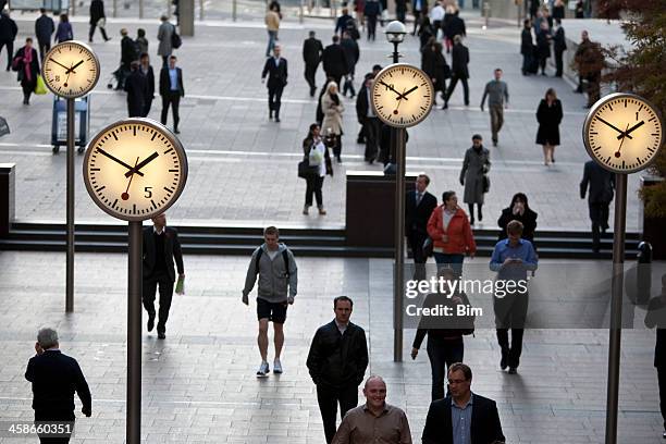 pedestrians walking past clocks in canary wharf london's financial district - beat the clock stock pictures, royalty-free photos & images