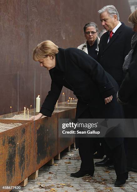 German Chancellor Angela Merkel places a candle as Berlin Mayor Klaus Wowereit looks on at the Berlin Wall Memorial at Bernauer Strasse on the 25th...