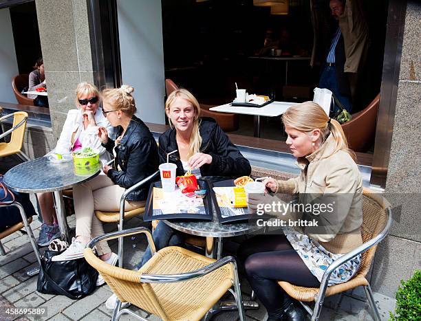 young women having a meal on the sidewalk outside mcdonalds. - mcdonalds restaurant stock pictures, royalty-free photos & images