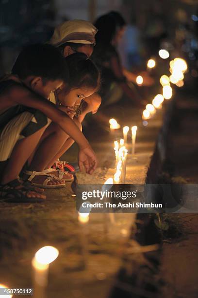 People sit around candles on the roadside during the candlelight memorial on November 8, 2014 in Tacloban, Leyte, Philippines. People lined the roads...