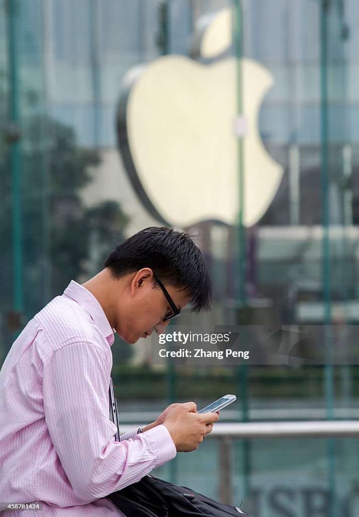 Outside an apple store, a young man is using his iPhone.