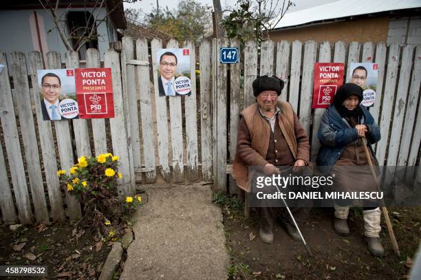 An elderly couple sits on a bench in front of the fence of their home covered with election campaign poster in support of Romanian Prime Minister...