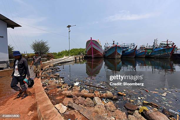 Men walk past a flooded path as fishing boats sit docked at a port in the Muara Baru area of North Jakarta, Indonesia, on Wednesday, Nov. 5, 2014....