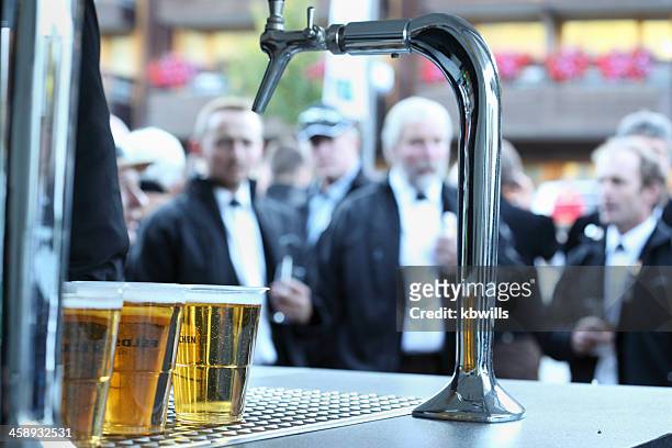 gläser bier an der bar mit formaler männer im hintergrund - bier zapfhahn stock-fotos und bilder