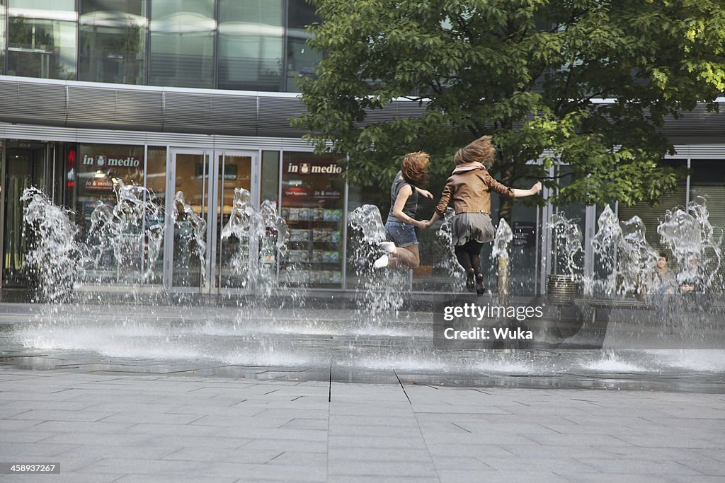 Two young girls jumping in the fountain