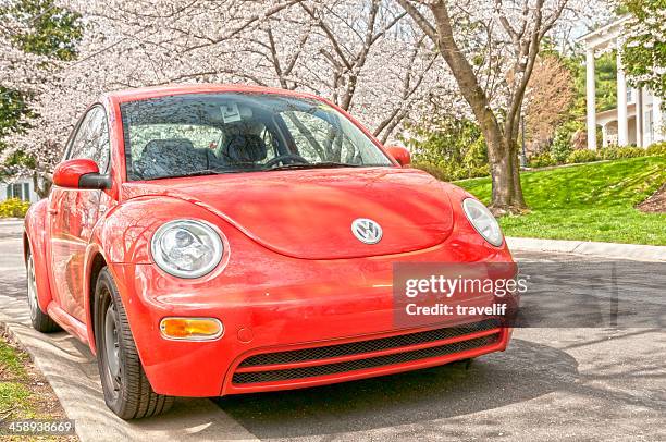 red volkswagen new beetle under blooming trees - beetle stock pictures, royalty-free photos & images