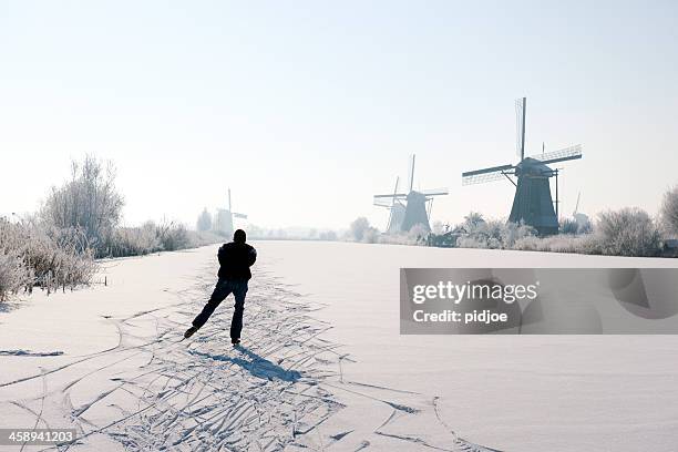 ice-skating man near windmills at kinderdijk in wintry landscape - kinderdijk stock pictures, royalty-free photos & images