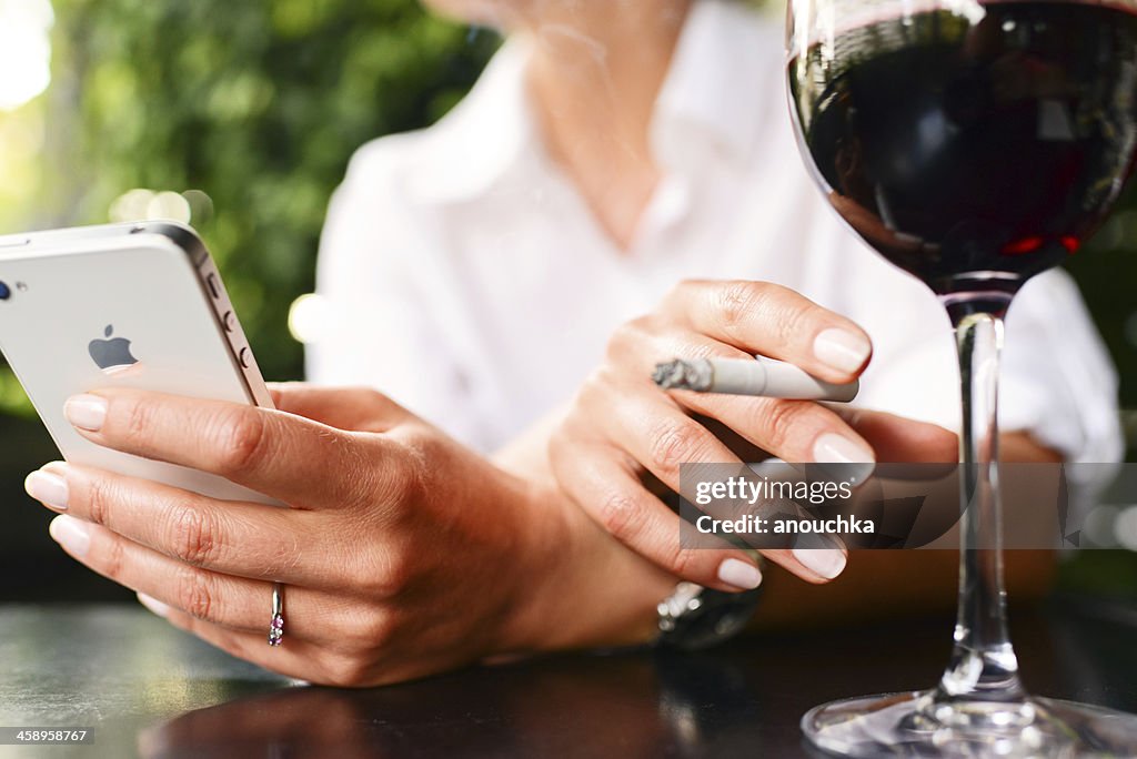 IPhone 4s, glass of wine and cigarette in woman hands