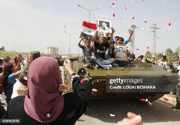 Syrian women shower army troops with rose petals and rice as youths holding up portraits of President Bashar al-Assad ride on an army tank pulling...
