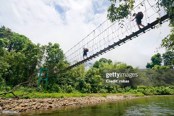 two tourists with backpacks crossing a suspension bridge. - gunung mulu national park stock pictures, royalty-free photos & images