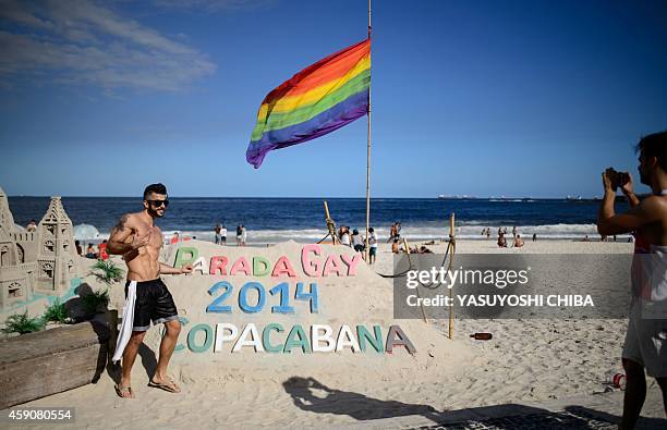 Man poses next to a sand sculpture during the annual Gay Pride Parade at Copacabana beach in Rio de Janeiro, Brazil, on November 16, 2014. AFP PHOTO...