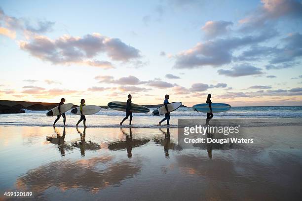 five surfers walk along beach with surf boards. - five people foto e immagini stock
