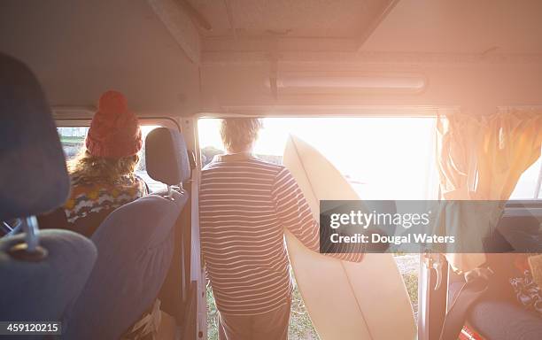 Surfing couple look out to sea from camper van.