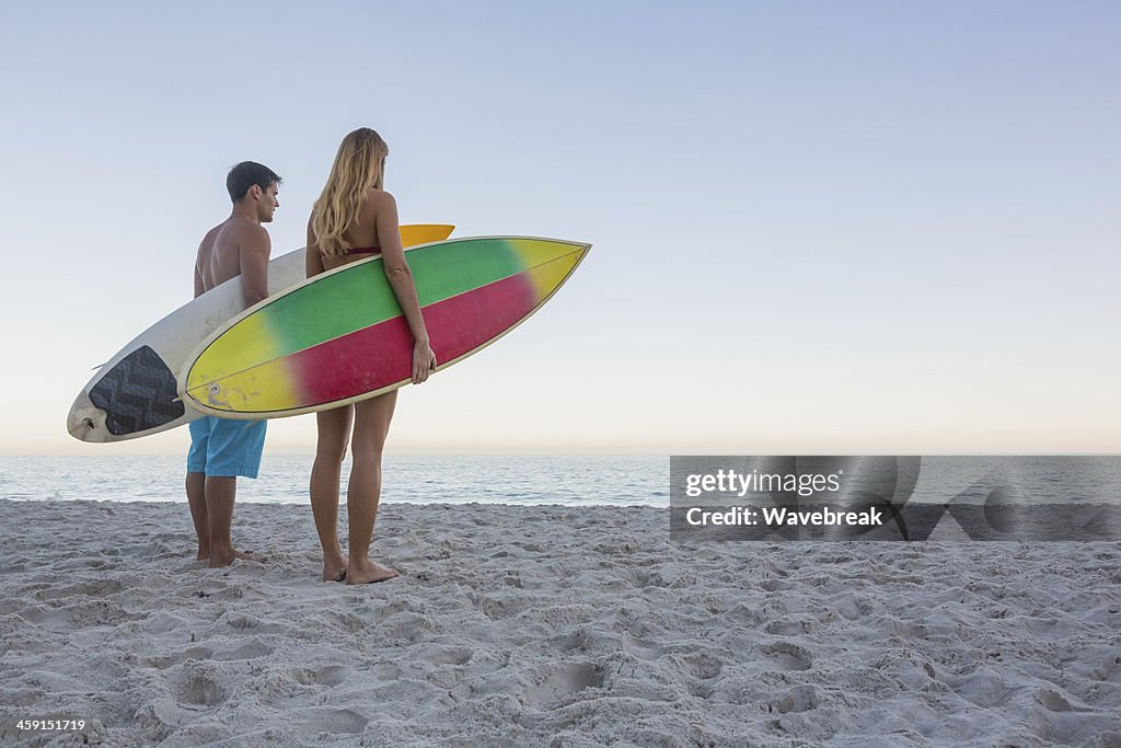 Thoughtful sporty couple holding their surfboards