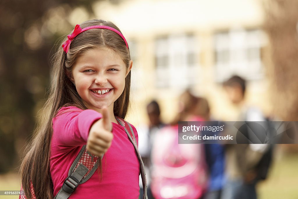 Schoolgirl in front of the school showing thumb-up