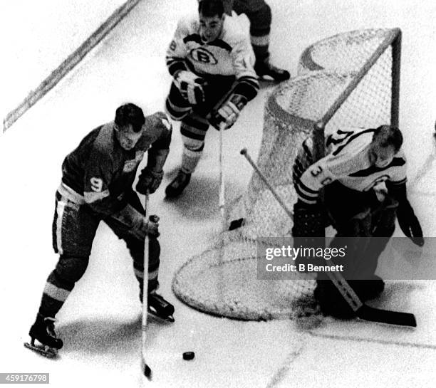 Gordie Howe of the Detroit Red Wings skates with the puck around the net as goalie Gerry Cheevers and Bob Woytowich of the Boston Bruins defend the...