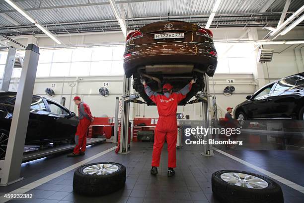 Mechanic checks an underside assembly at the rear of a Toyota Vento vehicle while raised on an hydraulic lift in the workshop at a Toyota Motor Corp....