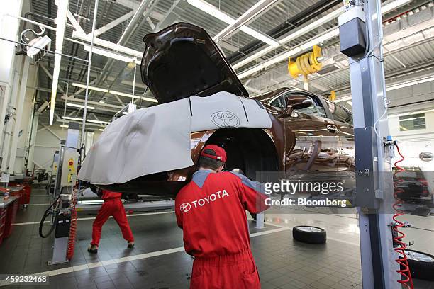 Mechanic works in the front wheel arch of a Toyota vehicle while raised on an hydraulic lift in the workshop at a Toyota Motor Corp. Automobile...