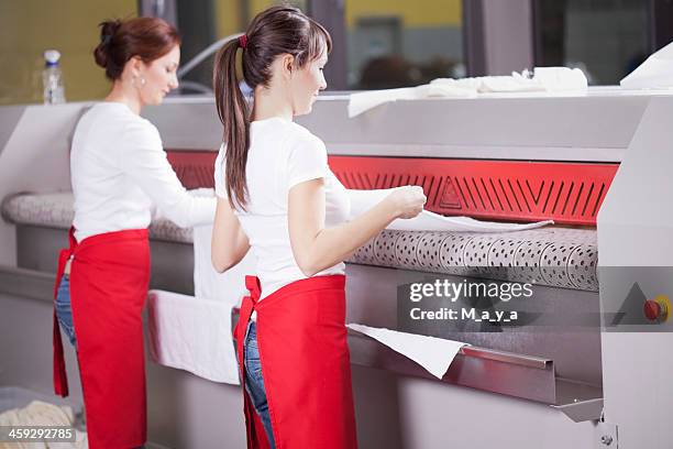 two women working on an industrial ironing machine  - washing mashine stock pictures, royalty-free photos & images