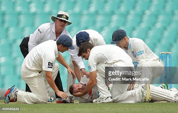 Phillip Hughes of South Australia is helped by New South Wales players after falling to the ground after being struck in the head by a delivery...