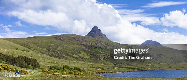 Tourists cycling by loch and Stac Pollaidh - Stack Polly - in glacier mountain range in the North West Highlands Geopark in Coigach region of...