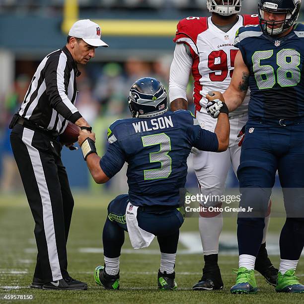 Quarterback Russell Wilson of the Seattle Seahawks is helped up by tackle Justin Britt and referee Gene Steratore against the Arizona Cardinals at...