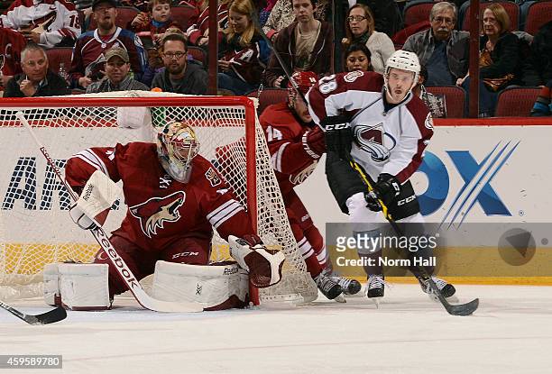 Paul Carey of the Colorado Avalanche works the puck around goaltender Mike Smith of the Arizona Coyotes as Joe Vitale of the Coyotes defends during...