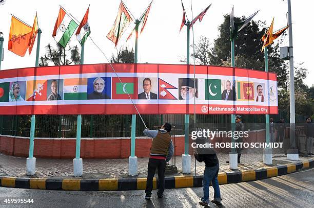 Two Nepalese workers use poles to untangle flags representing the SAARC nations near the main entrance of the venue hosting the opening session of...